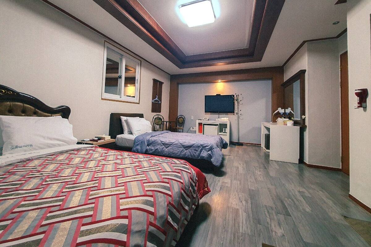 A hotel room with a large bed, a smaller bed, a desk, a TV, and a mirror.
