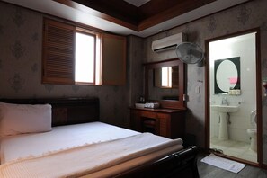 A bedroom with a bed, a dresser, a mirror, and a bathroom visible through an open door. - Galleria Hotel (Andong)