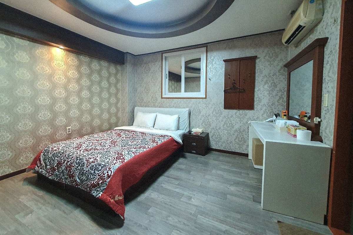 A bedroom with a bed, a dresser, a mirror, and a ceiling light.