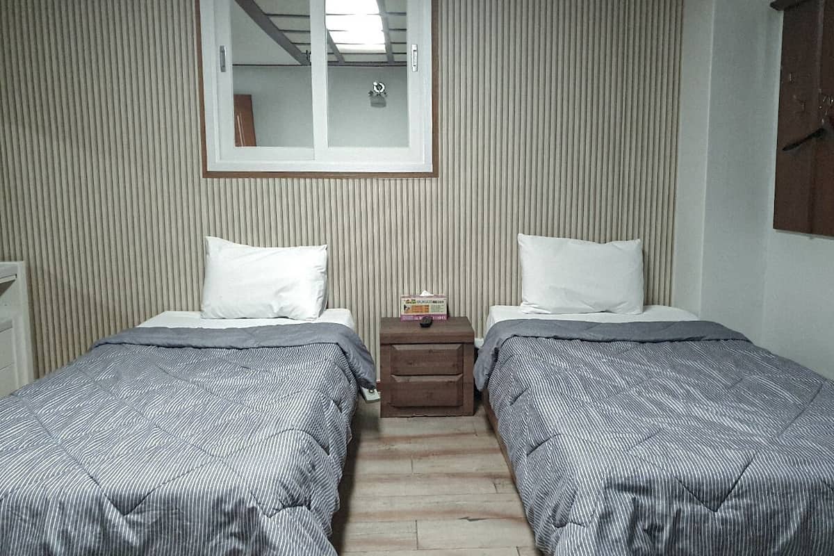 A small, neatly arranged bedroom with two beds, a nightstand, and a window.
