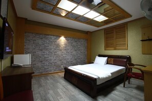 A bedroom with a bed, a desk, a chair, a stone wall, and a skylight. - Galleria Hotel (Andong)