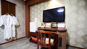 Habitación de hotel con escritorio de madera, televisor de pantalla plana, teléfono, refrigerador pequeño y una silla.