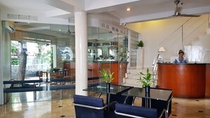 Un vestíbulo de hotel con una recepción, una escalera y un separador de vidrio que divide el vestíbulo del comedor.