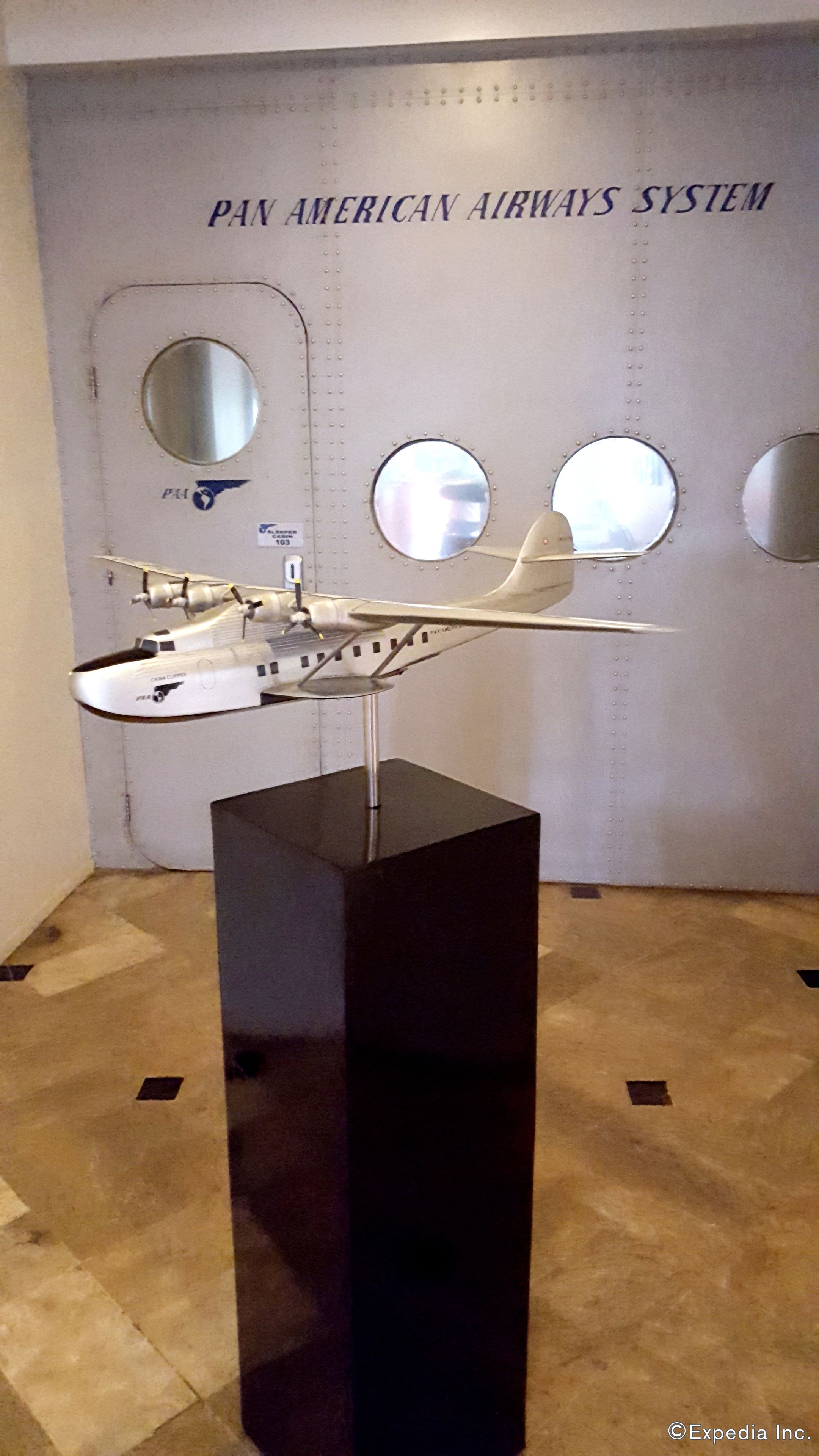 Een modelvliegtuig tentoongesteld voor een muur met de tekst 'PAN AMERICAN AIRWAYS SYSTEM'.