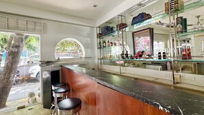 Una zona de bar con mostrador de madera, taburetes y estantes con botellas y vasos.