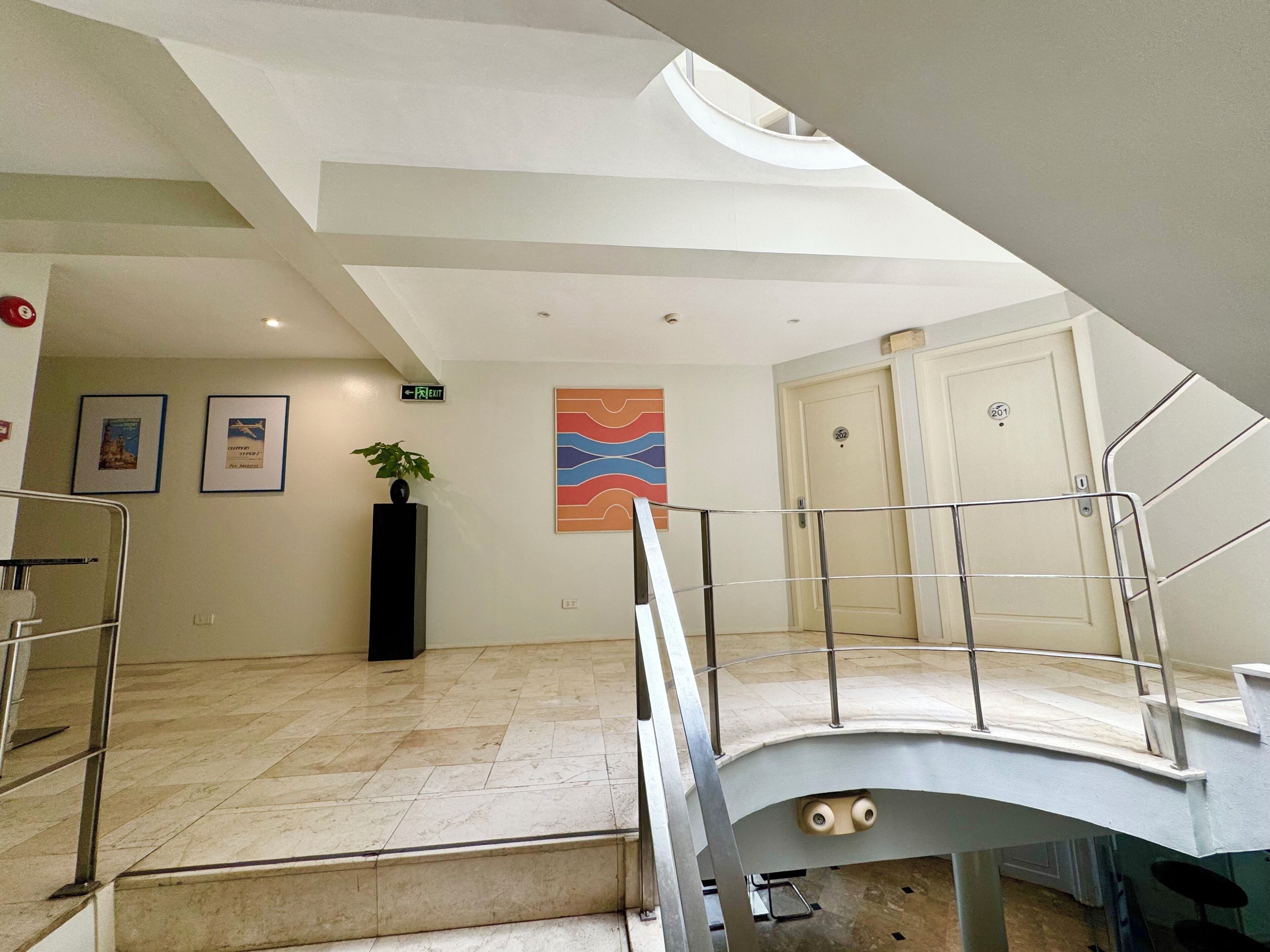 Una hall moderna di un hotel con una scala, una pianta in vaso, quadri appesi al muro e un'opera d'arte astratta dai colori vivaci.