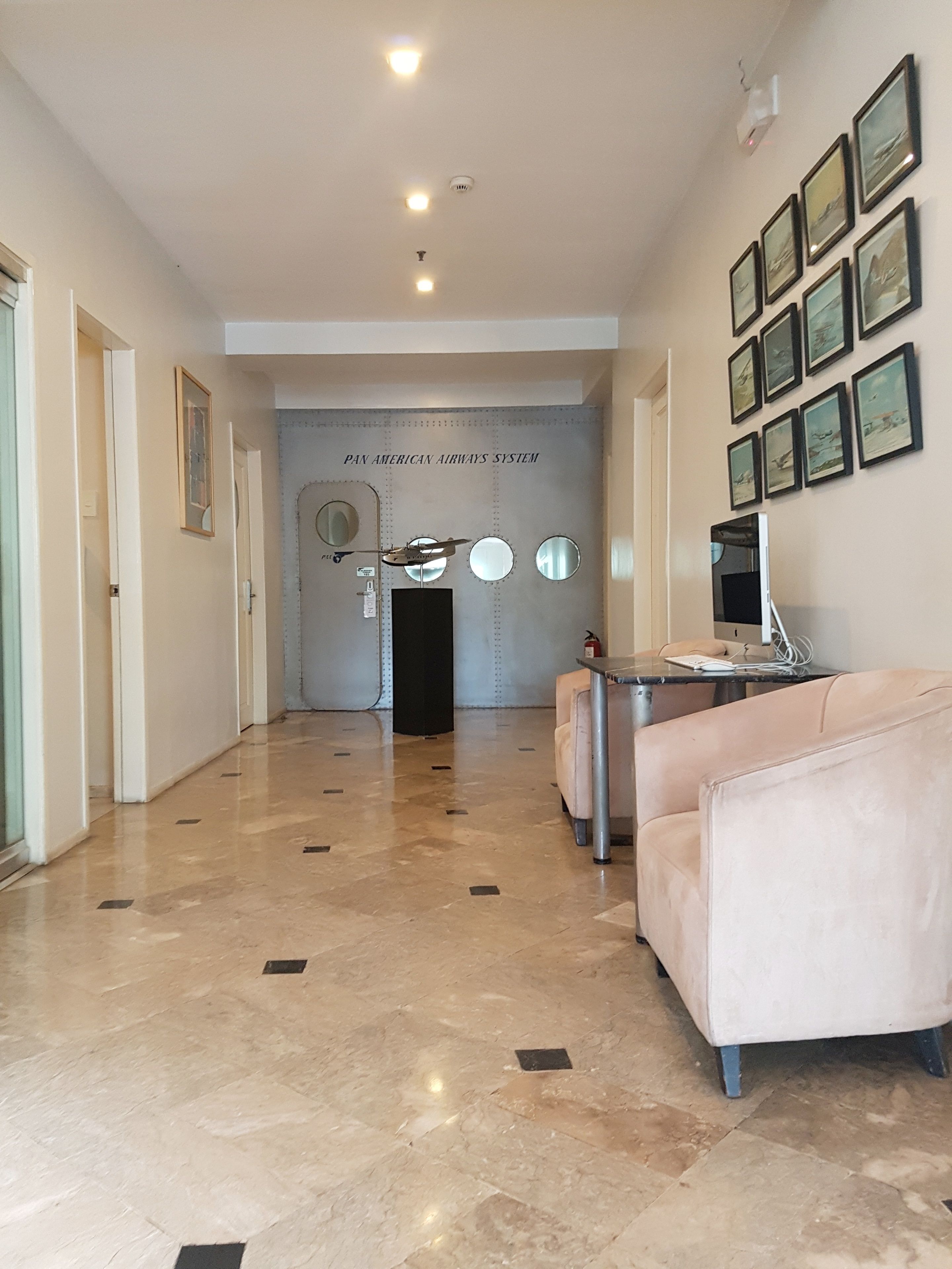 A hallway with a polished marble floor, a reception desk, a seating area with a sofa, and a wall with framed pictures.