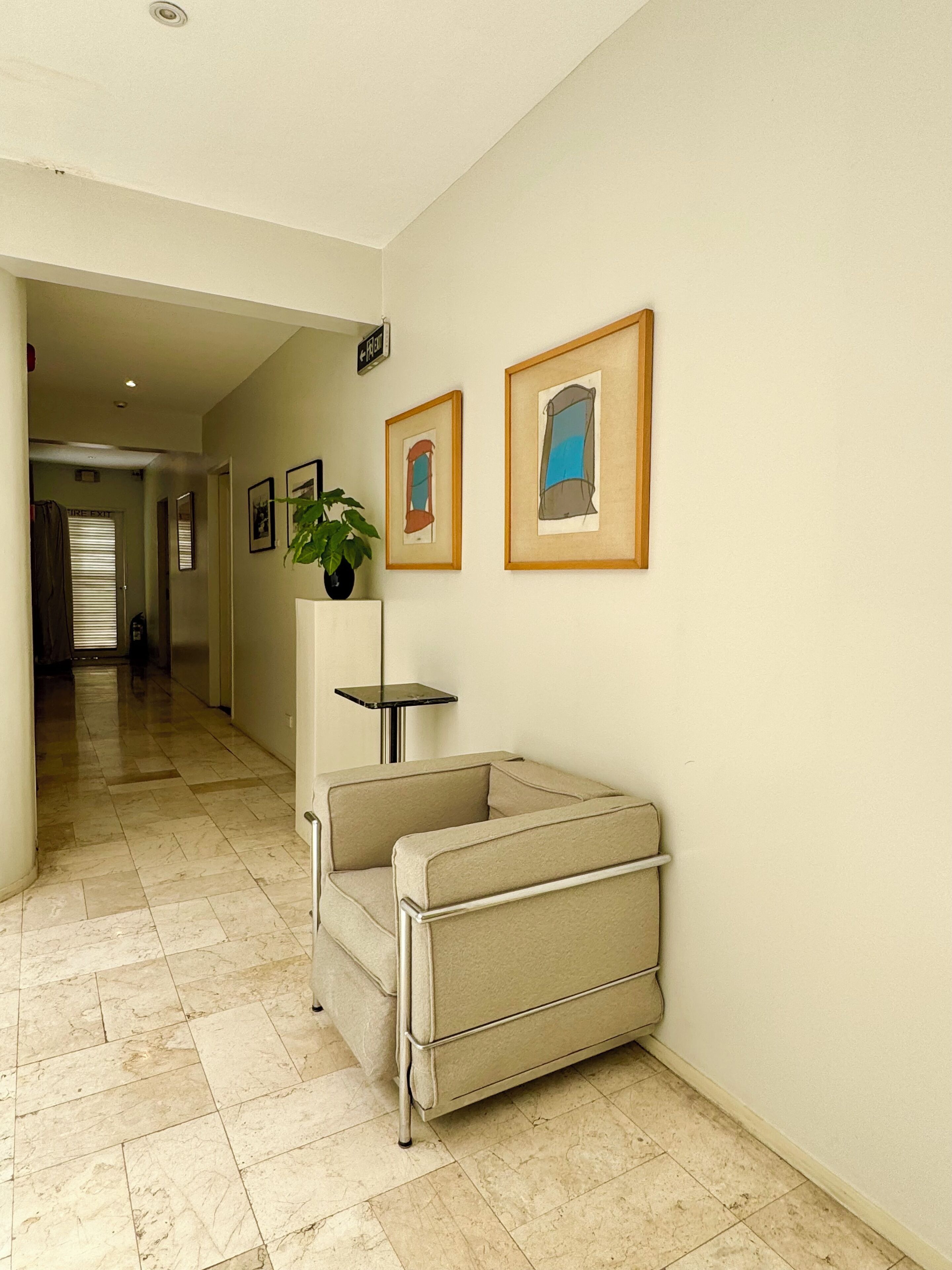 Un couloir avec un canapé beige, une petite table et des œuvres d’art encadrées accrochées au mur.