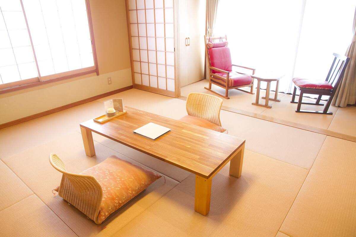 Una habitación japonesa tradicional con suelo de tatami, una mesa de madera baja y dos sillas con cojines.