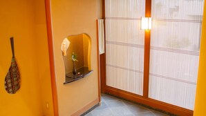 Un interior japonés tradicional con suelo de tatami, un biombo shoji y un pequeño estante con un jarrón.