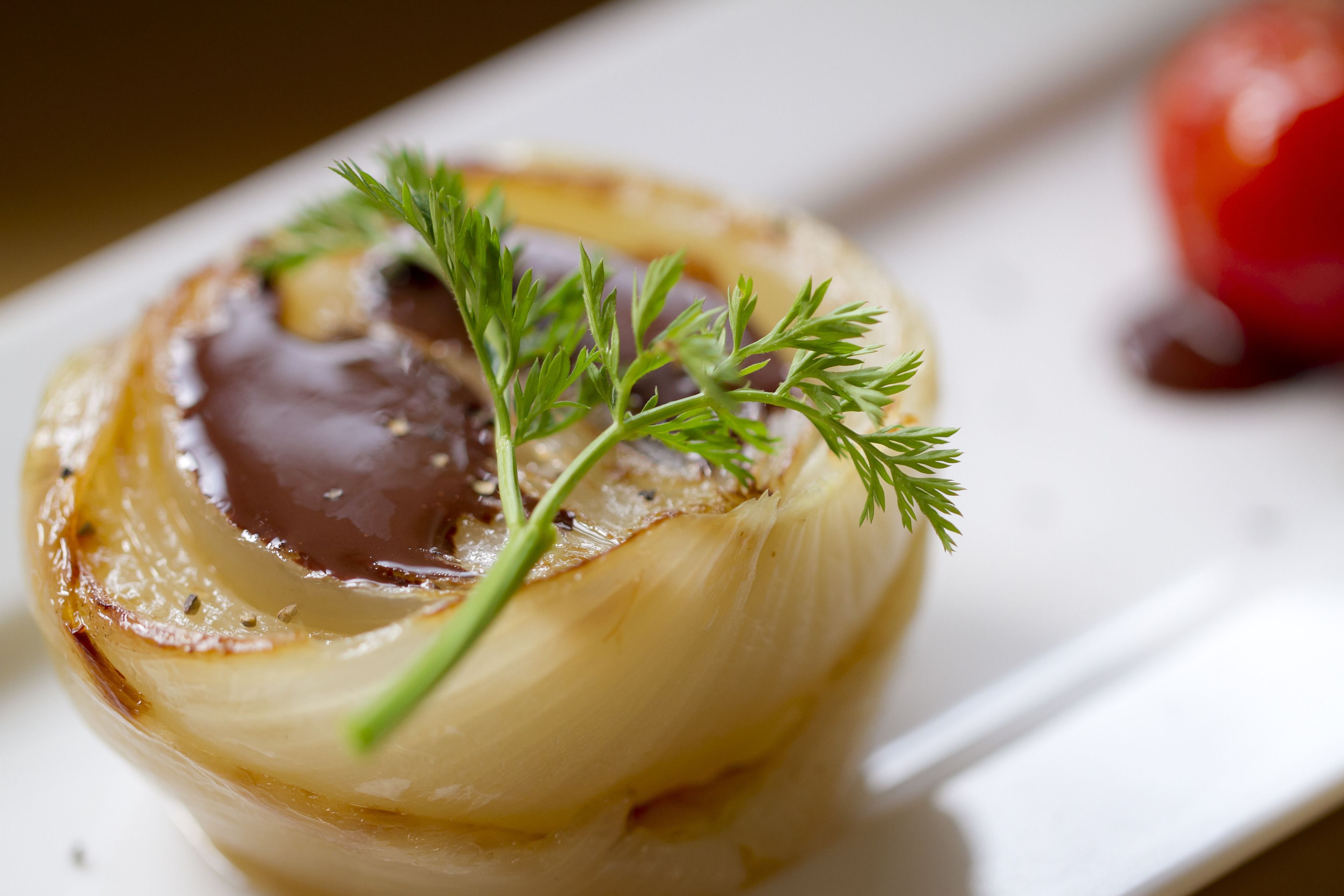 A close-up of a dish with a cooked onion, a dollop of sauce, and a sprig of dill.