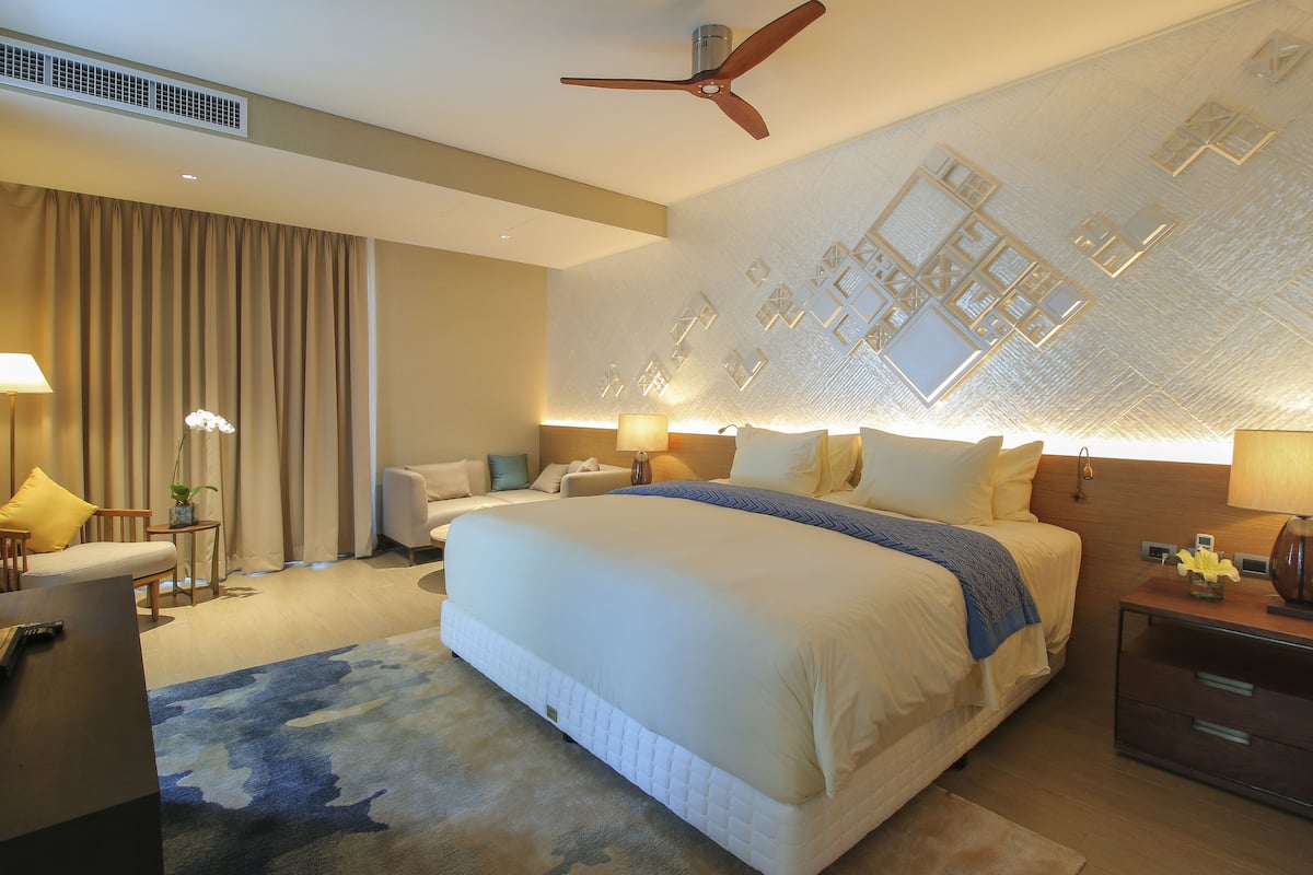 A modern hotel room with a large bed, a ceiling fan, and a decorative wall panel.