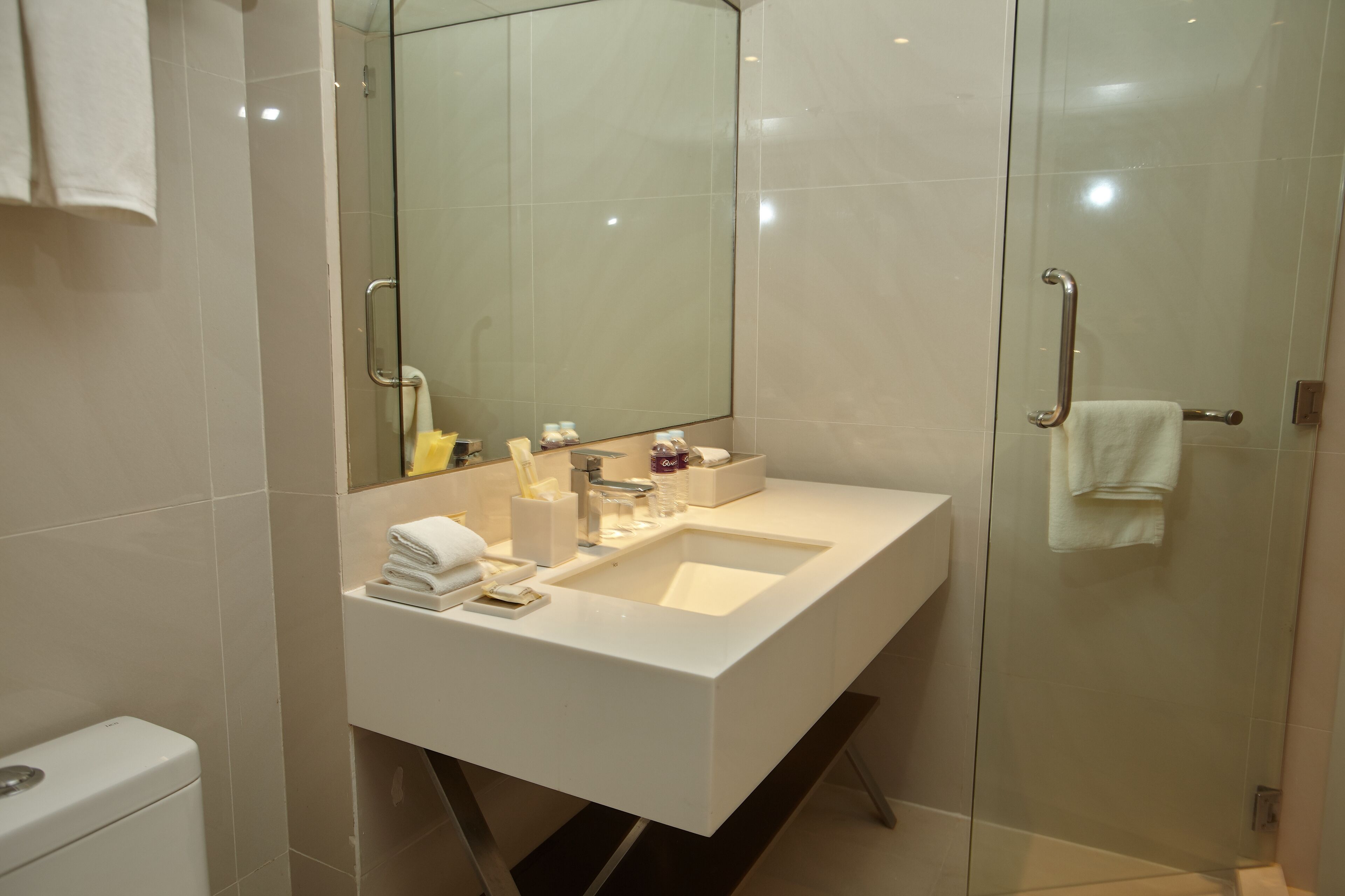 Un baño moderno con lavamanos blanco, cabina de ducha de vidrio y un espejo grande.