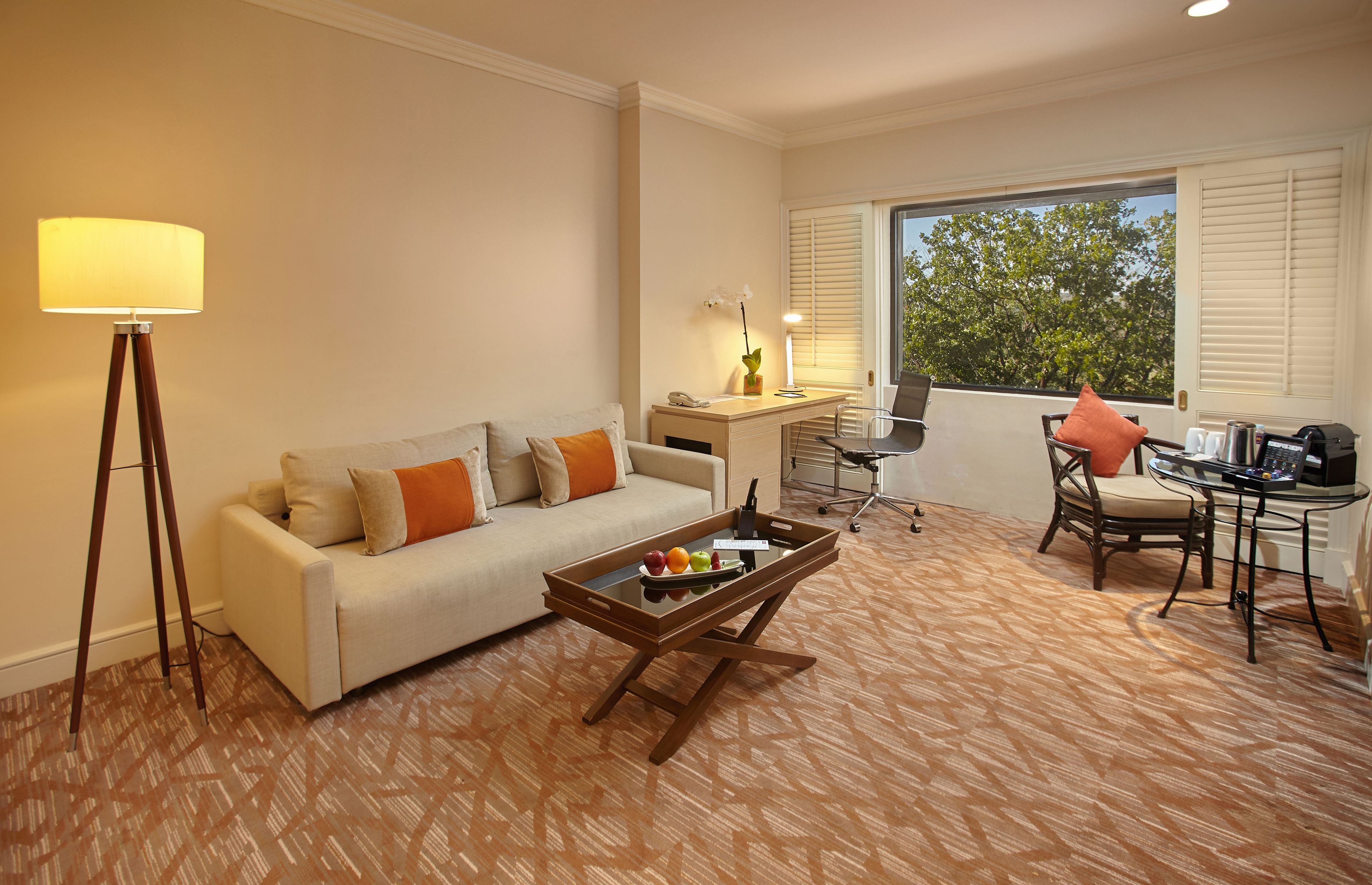 Una habitación de hotel con sofá, mesa de centro, escritorio, silla y un ventanal grande.