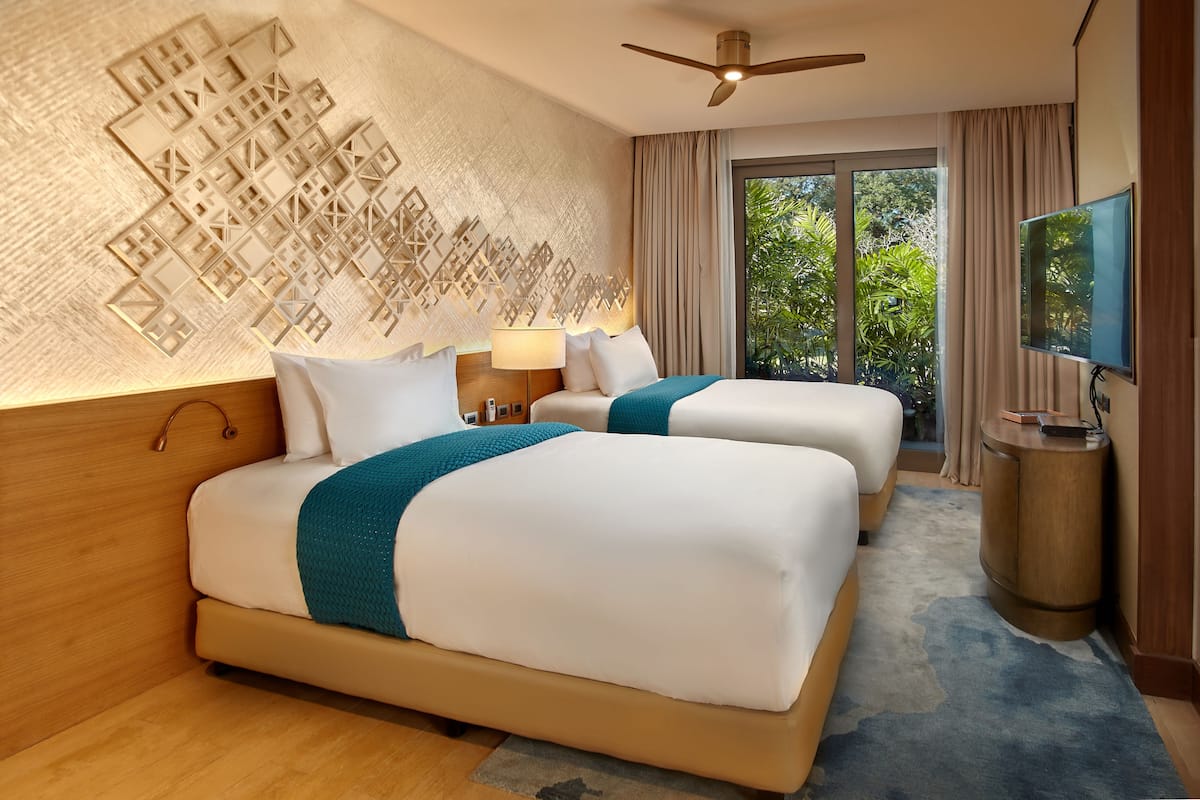 A hotel room with two beds, a ceiling fan, a TV, and a large window with curtains.