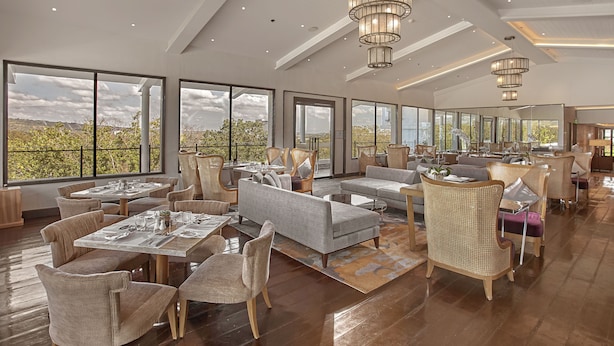 Un amplio espacio interior con ventanas grandes, una zona de comedor y un área de estar con sofás y sillones.