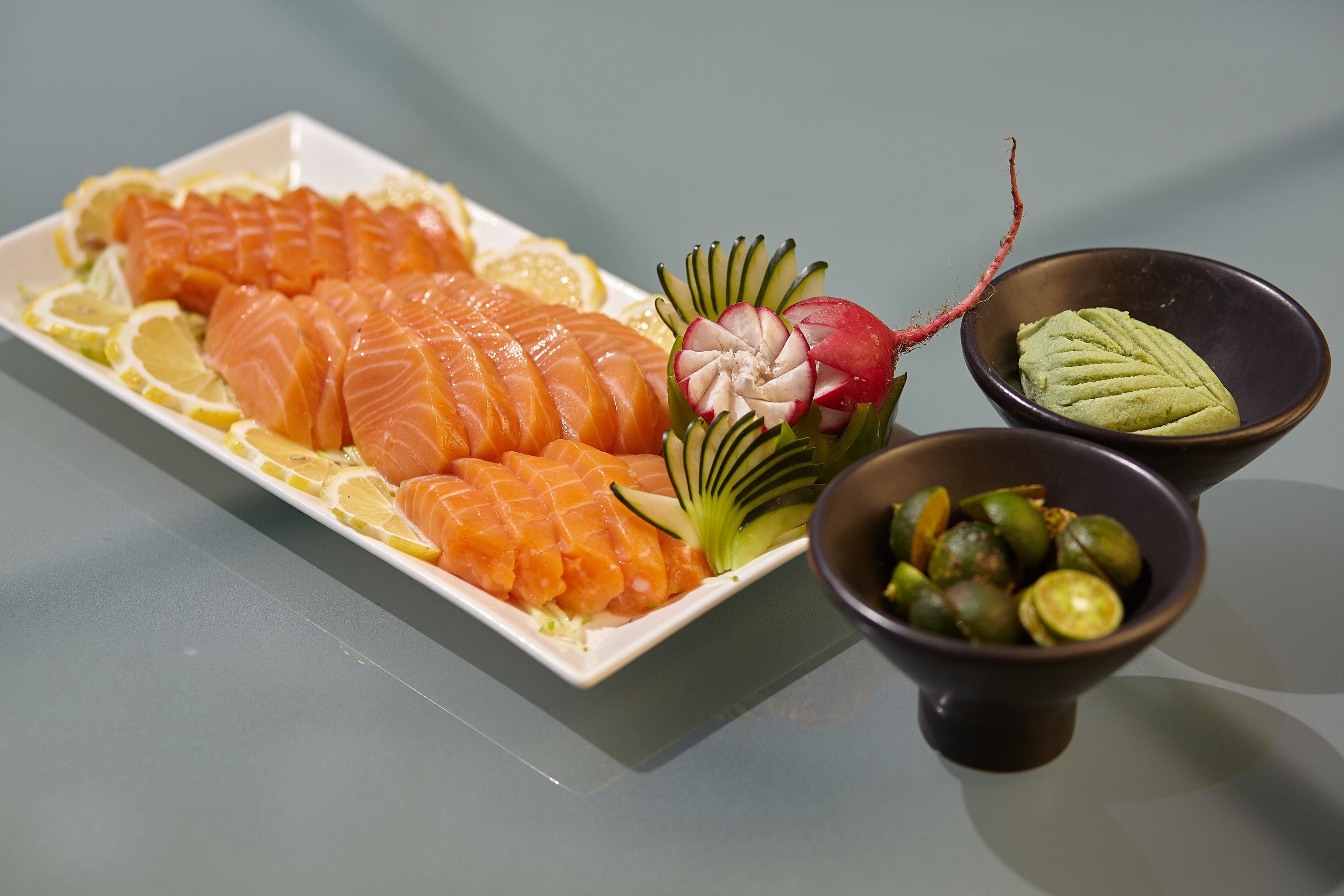 Une assiette de tranches de saumon, garnie de citron et de radis, et deux petits bols contenant des légumes verts.