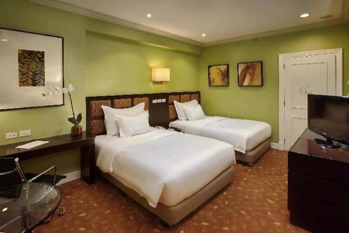 A hotel room with two beds, a television, a desk, and artwork on the walls.