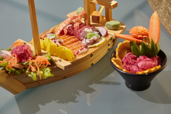 Un bateau en bois rempli de divers fruits de mer et légumes, et une coupe de crème glacée surmontée d’une fleur décorative.