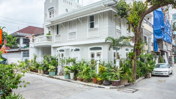 Un bâtiment blanc à deux étages, doté de balcons et entouré de plantes en pot.