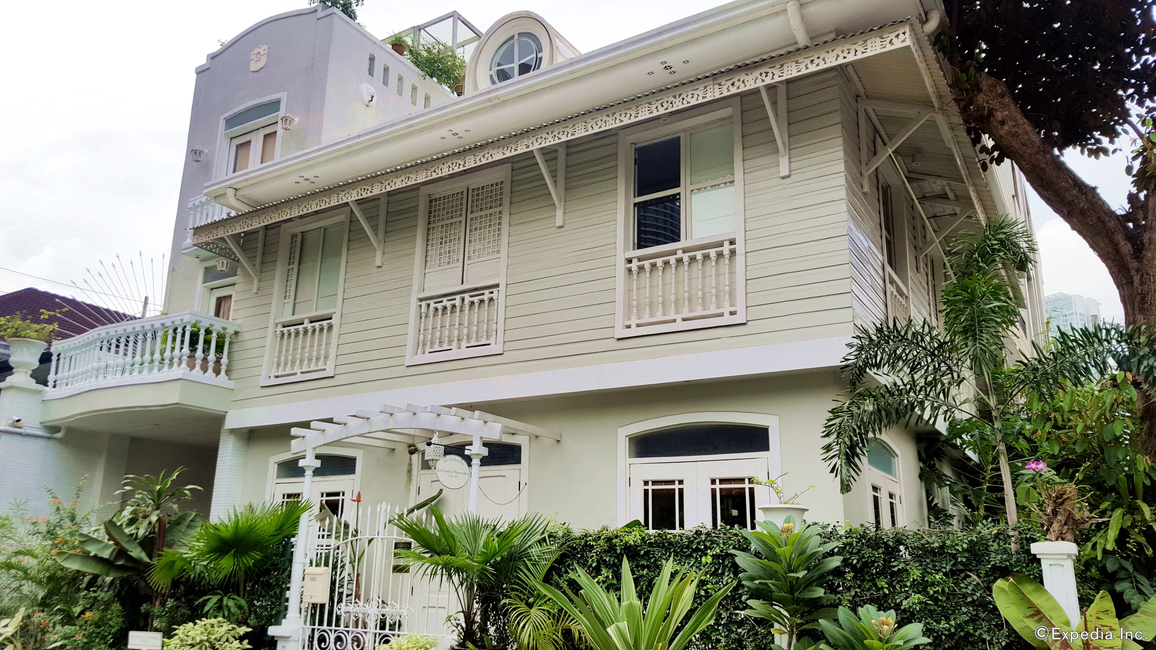 A two-story colonial-style building with a balcony, a gated entrance, and lush greenery.