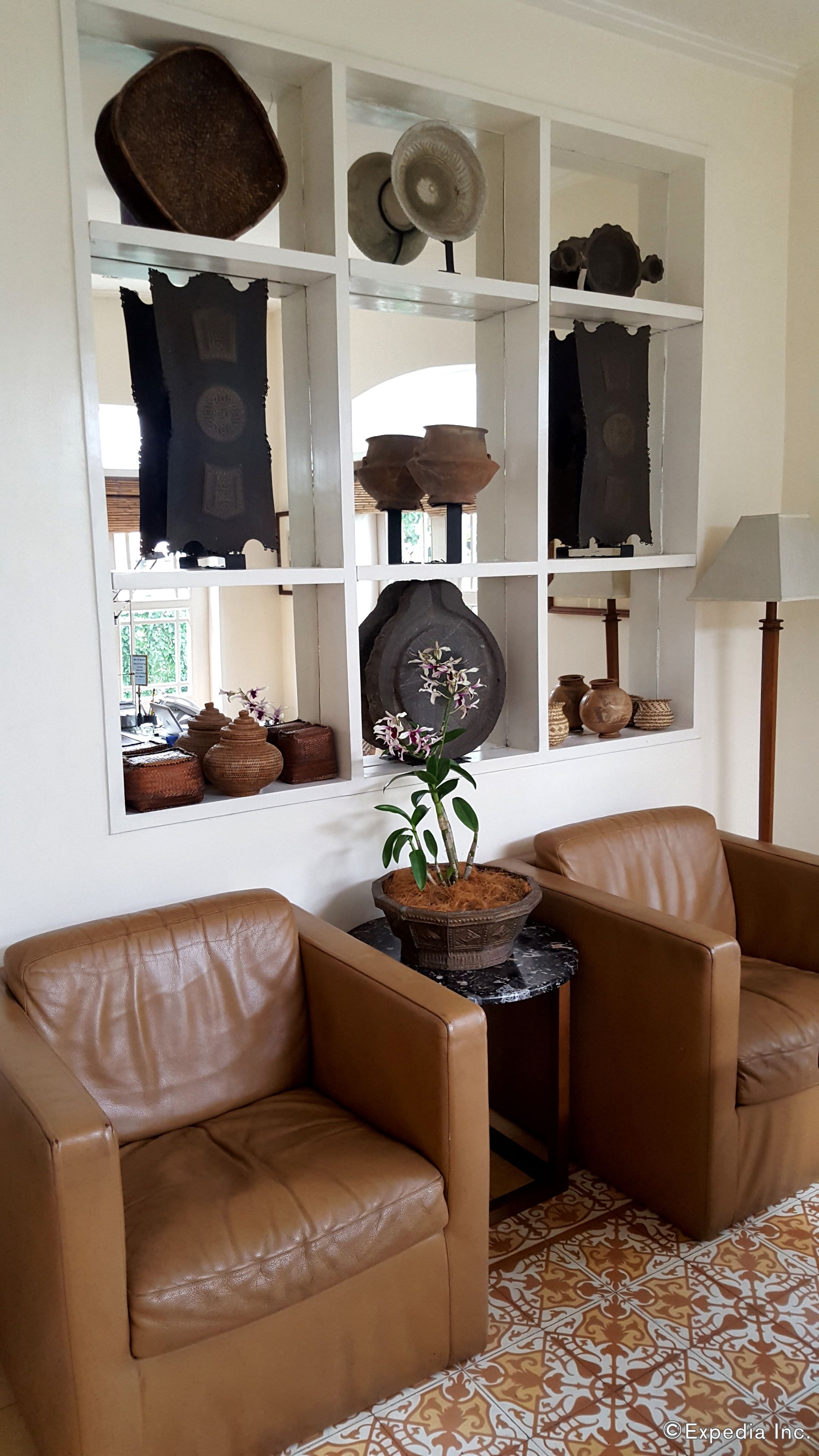 Un salon avec des fauteuils en cuir marron, une petite table et une étagère ornée d’objets décoratifs.