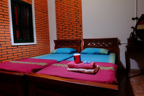 Una habitación con dos camas, un muro de ladrillo, una ventana con contraventanas verdes y un cabecero de madera.