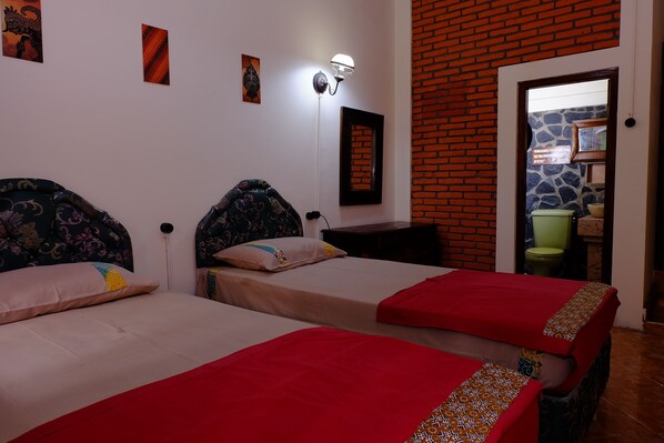 Habitación de hotel con dos camas, un muro de ladrillo y un espejo.