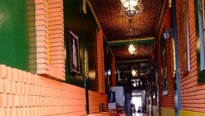A corridor with a checkered floor, wooden chairs, and tables with tablecloths. - Kampoeng Djawa Guesthouse (Yogyakarta)