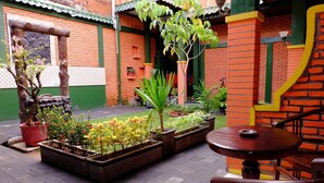 A courtyard with brick walls, potted plants, and a wooden table and chair. - Kampoeng Djawa Guesthouse (Yogyakarta)