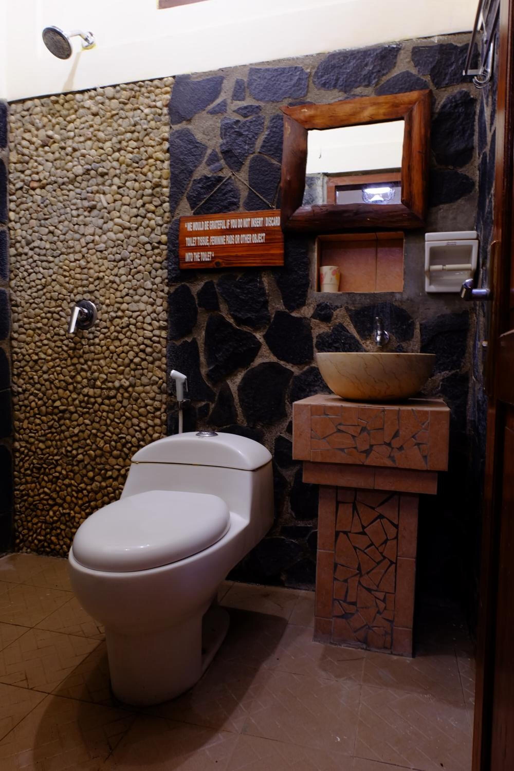 Une salle de bain avec un mur en pierre, un meuble-lavabo en bois doté d’un vasque, des toilettes et un miroir.