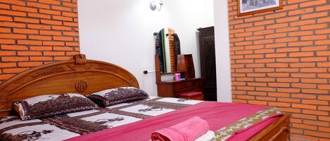 A neatly made bed with a red blanket and a pink towel, a wooden headboard, and a brick-patterned wall.