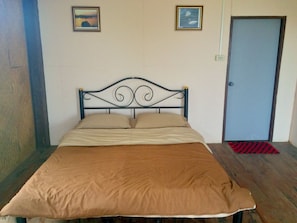 A single bed with a metal headboard, two pillows, and a brown bedspread in a room with a door and two framed pictures on the wall. - Tony Guesthouse (Pai)