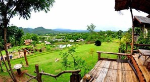 A rustic wooden deck overlooking a lush green landscape with a river and distant hills. - Tony Guesthouse (Pai)