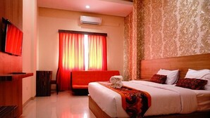 A hotel room with a large bed, a sofa, a TV, and a window with curtains. - New d'Dhave Hotel (Padang)
