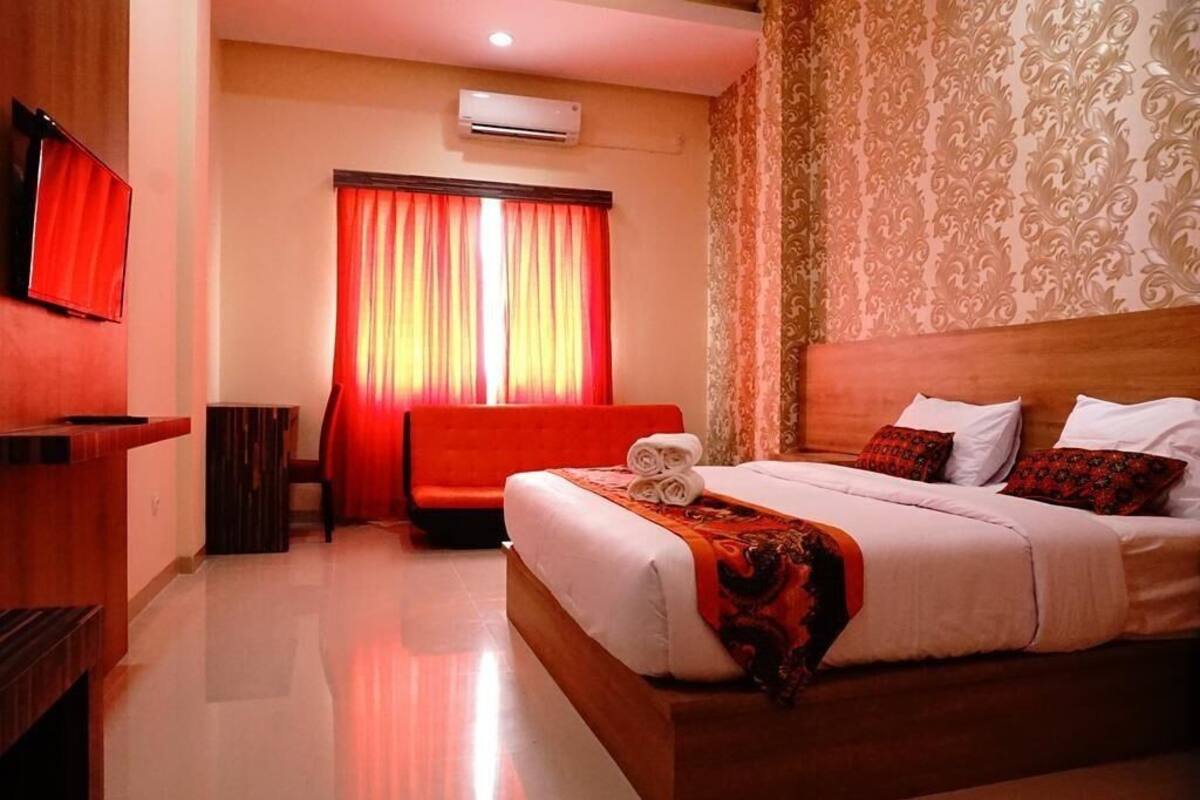 Una habitación de hotel con una cama grande, un sofá, un televisor y una ventana con cortinas.