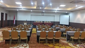 A conference room with rows of tables and chairs, a podium, and a projection screen. - New d'Dhave Hotel (Padang)