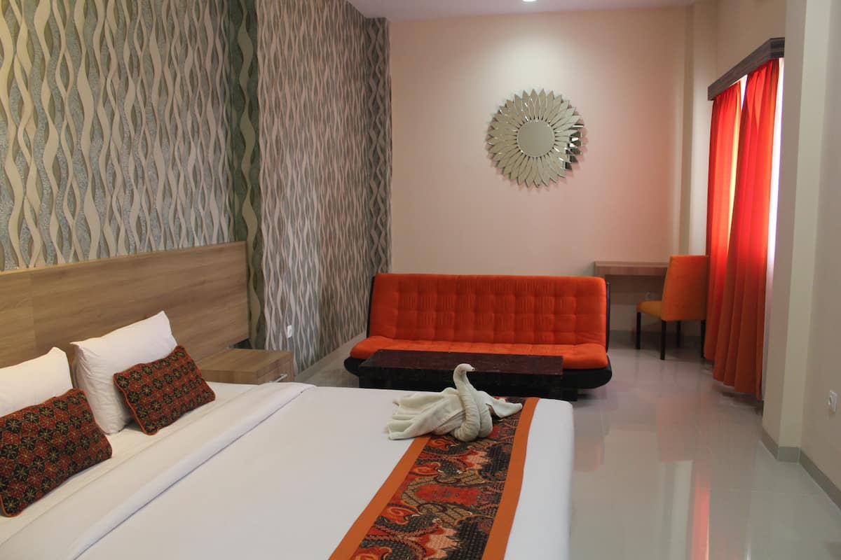 Una habitación de hotel con cama, un sofá rojo, una pared con espejo decorativo y una ventana con cortinas rojas.
