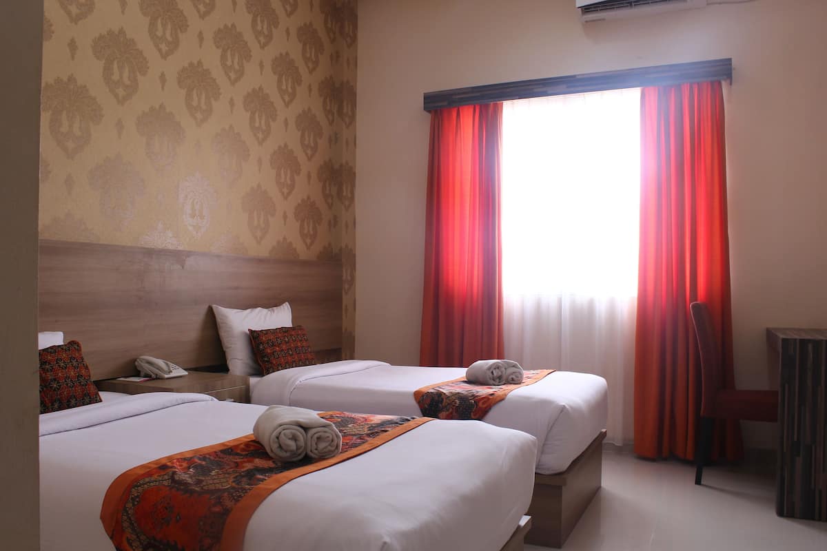 Una habitación de hotel con dos camas, un cabecero de madera, un teléfono y una silla.