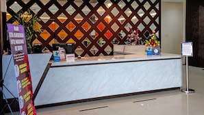 A reception desk with a modern design, a decorative wall with diamond patterns, and a signboard on the left. - New d'Dhave Hotel (Padang)