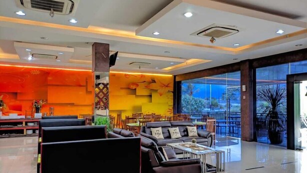 A spacious lobby with a modern design, featuring a seating area with sofas and tables, a large window with a view of the outdoors, and a decorative wall with abstract patterns. - New d'Dhave Hotel (Padang)