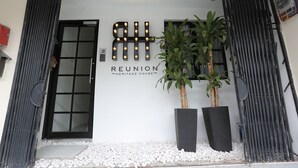 A building entrance with a sign reading "RTH Reunion Heritage House" and two potted plants. - Reunion Heritage House (George Town)
