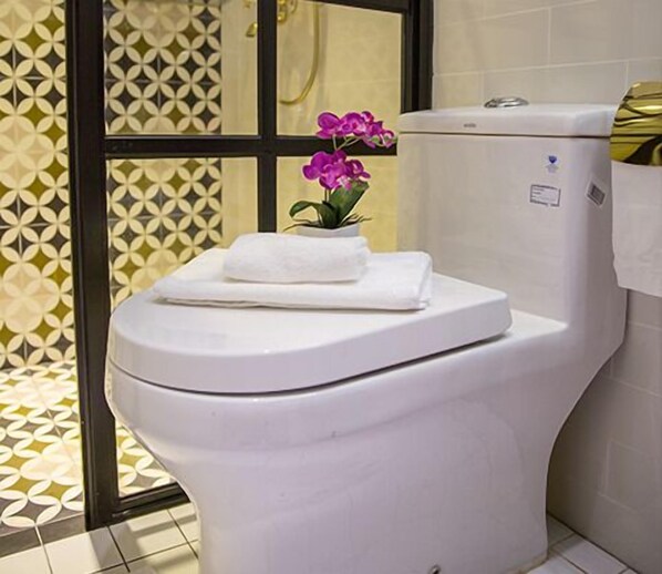 A toilet with a white seat and lid, a small potted orchid, and a towel on top. - Reunion Heritage House (George Town)