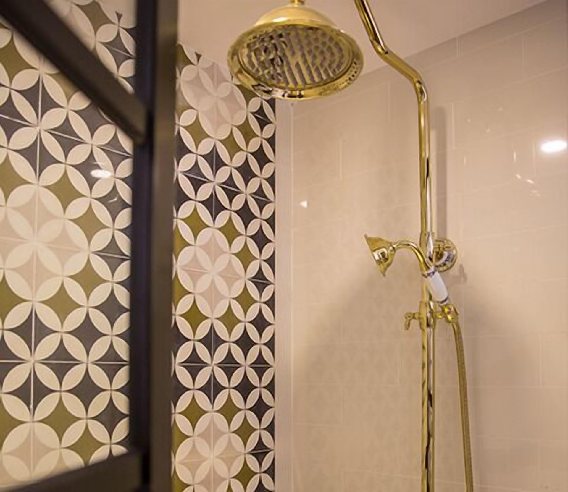 A shower with a gold showerhead and a wall with a geometric tile pattern.