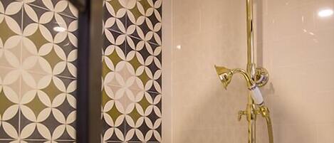 A shower with a gold showerhead and a wall with a geometric tile pattern.