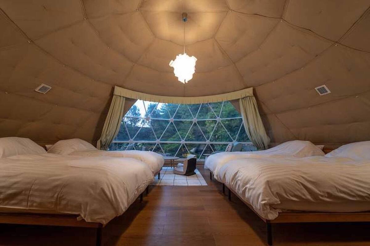 A dome-shaped room with two beds, a central table, and a large window.