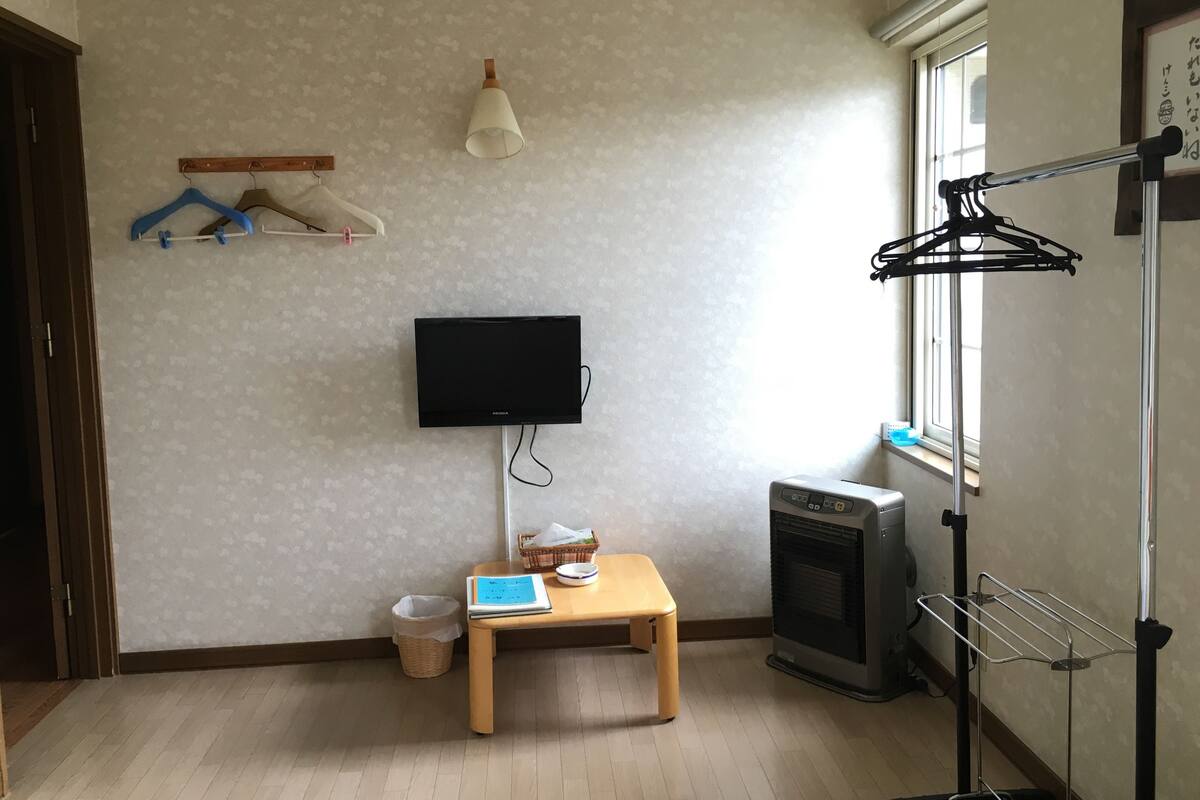 Une pièce avec un téléviseur fixé au mur, une petite table en bois sur laquelle se trouvent un panier et un carnet, un radiateur et un étendoir à linge.