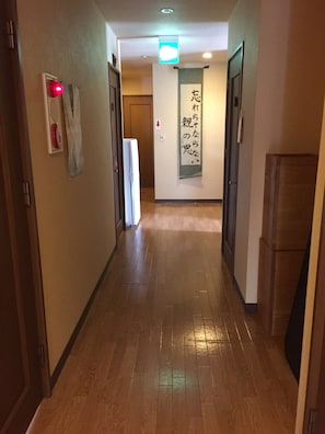 Un pasillo con suelo de madera, un cartel en la pared con caracteres japoneses y una puerta al final.
