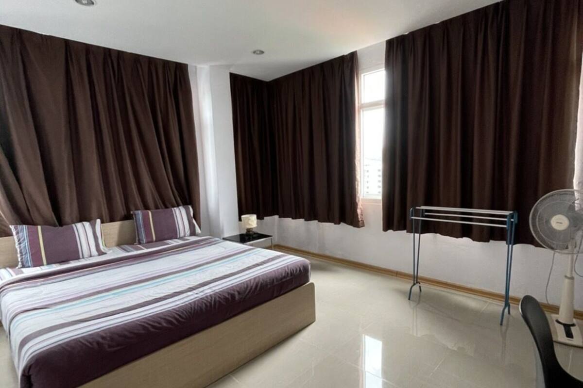 Una habitación de hotel moderna con una cama grande, un escritorio, una silla y un ventilador de pie.