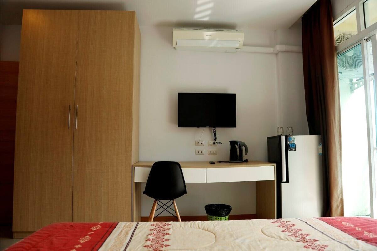 Habitación de hotel con armario de madera, escritorio con televisor de pantalla plana, hervidor, refrigerador y cama con colcha roja y blanca.